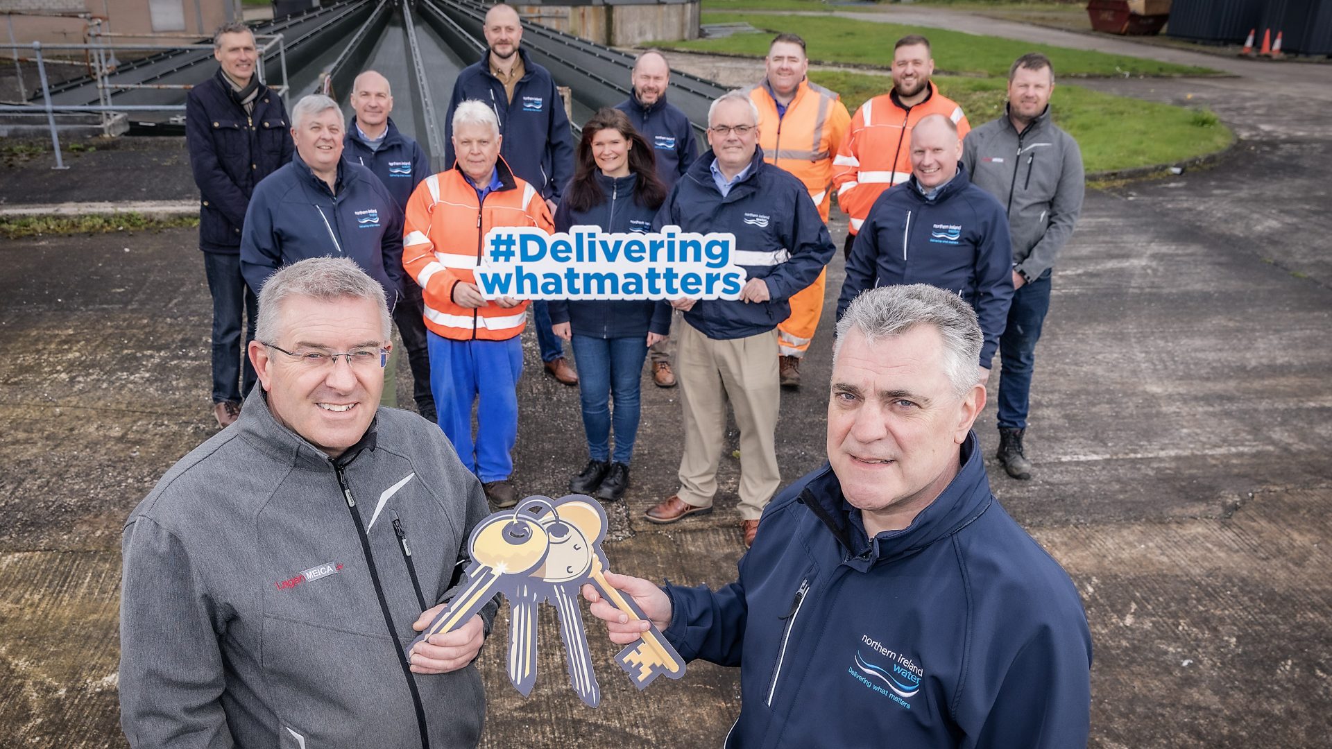 NI Water’s Ciaran Crozier (right) and Neil McKenzie from Lagan SCG in the foreground, as Neil hands over the keys to Ciaran. Transition team staff from NI Water and Lagan SCG in background.