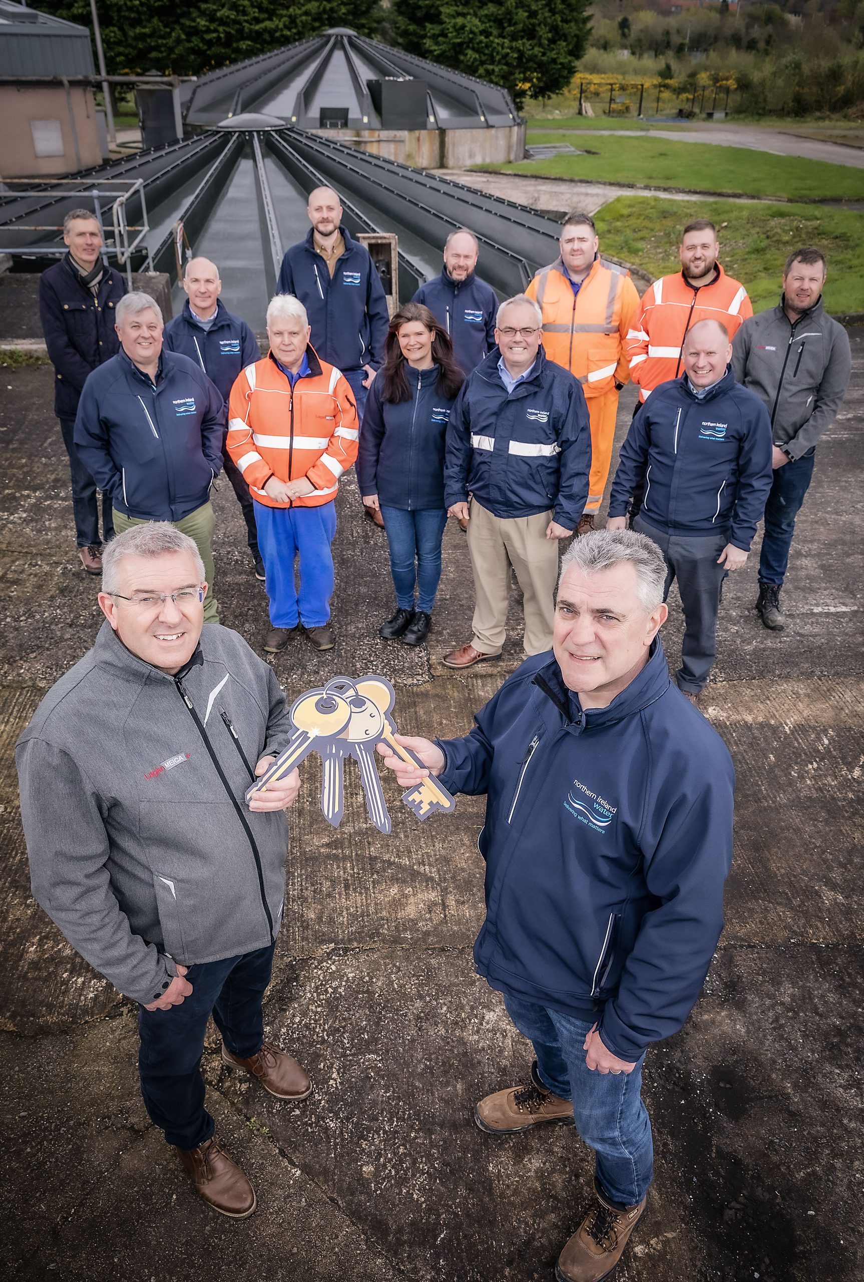 NI Water’s Ciaran Crozier (right) and Neil McKenzie from Lagan SCG in the foreground, as Neil hands over the keys to Ciaran.Transition team staff from NI Water and Lagan SCG in background.